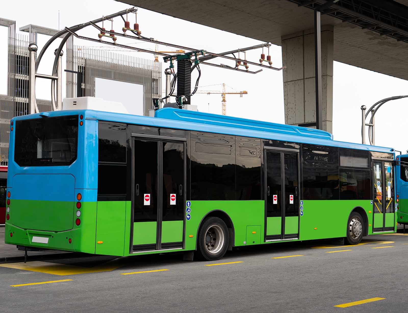 An EV city bus charges at an overhead pantograph charging station